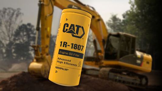 Cat oil filter with blurred excavator in background.