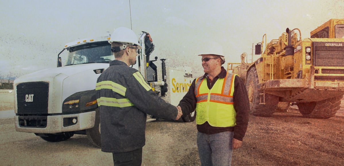Workers shaking hands in front of service vehicle and mining machine