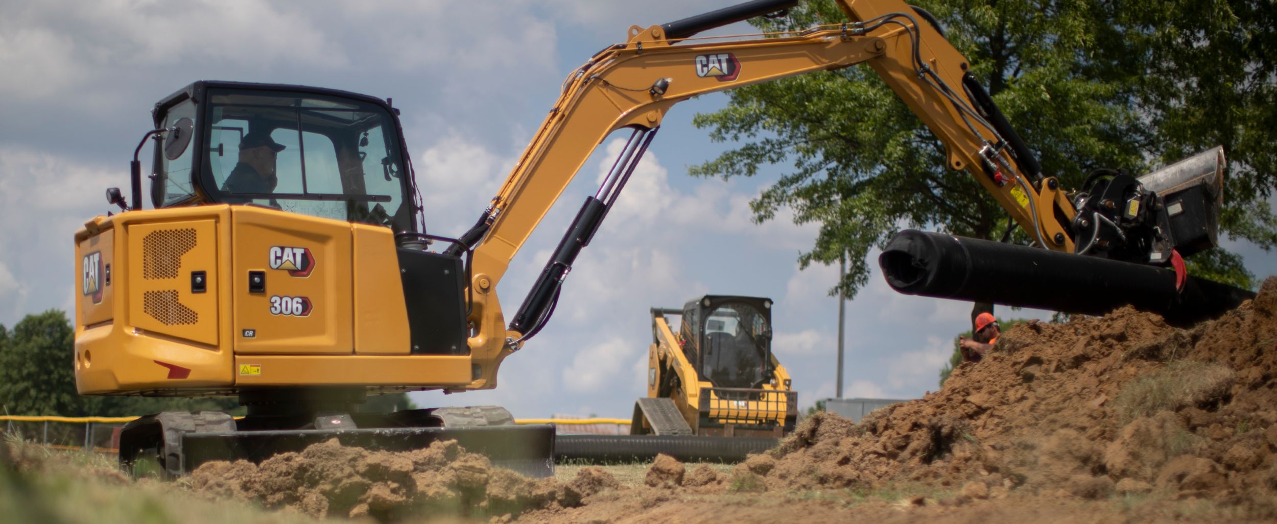 Mini excavator 306 digging dirt with a compact track loader in the background