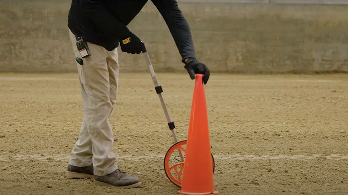person holding a measuring device and moving an orange traffic cone